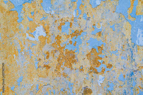 Fragment of a wall with old plaster. Traces of layers of paint of different colors are visible on the surface. Blue and yellow. Background. Texture.