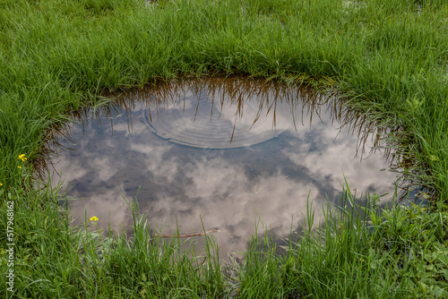 Manhole cover in the reflection of clouds in a puddle