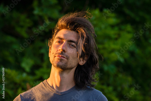 Portrait of happy young man looking at camera outdoor. beard feeling confident at sunset. Closeup nature background. summer day long hair Handsome grey shirt sexy finger up thumbs up smiling