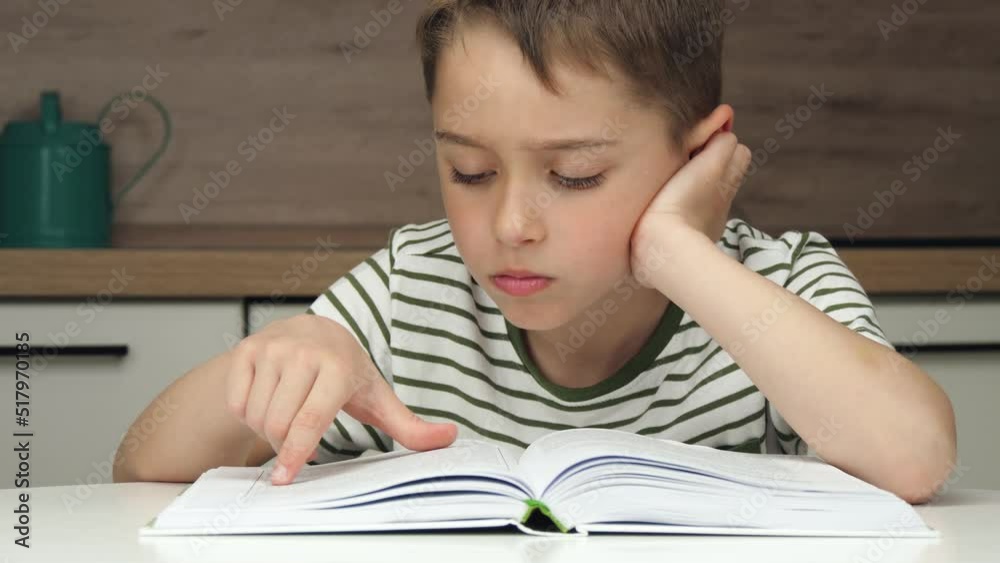 Portrait of a boy enthusiastically reading a book sitting at a table at home schooling. The concept of distance education. kid and book Portrait of a boy enthusiastically reading a book sitting at a table at home schooling. The concept of distance education. kid and book
