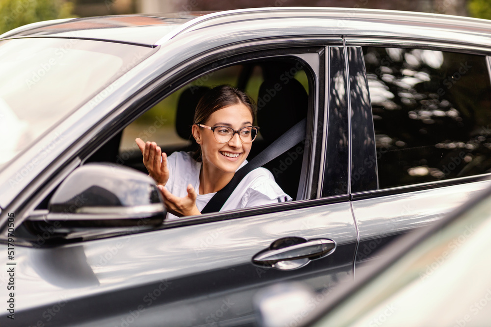 A young woman is sitting in her car in traffic and talking to another driver in the car. She respects traffic regulations. A girl in a car in traffic