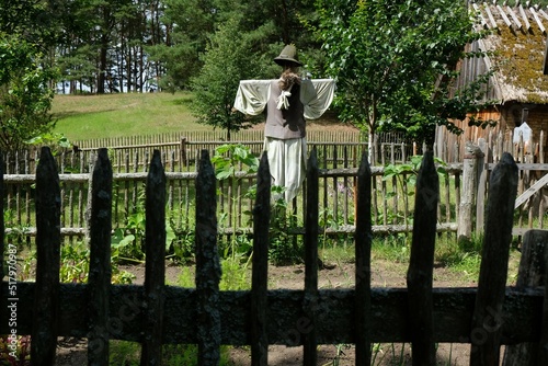 Scarecrow in a garden in the countryside by a wooden fence and cottages. Wdzydze Kiszewskie, Kashubia, Poland