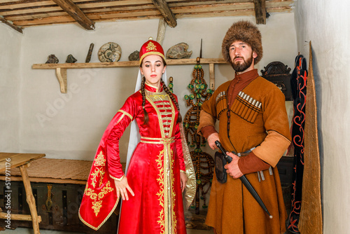 A young couple a man and a girl in Caucasian Circassian national costumes stand inside their traditional old house in the village photo