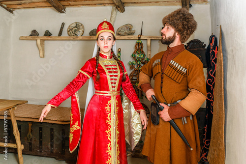 A young couple a man and a girl in Caucasian Circassian national costumes stand inside their traditional old house in the village