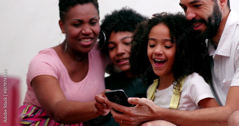 Obraz premium Interracial family and kids laughing together looking at cellphone at home sofa
