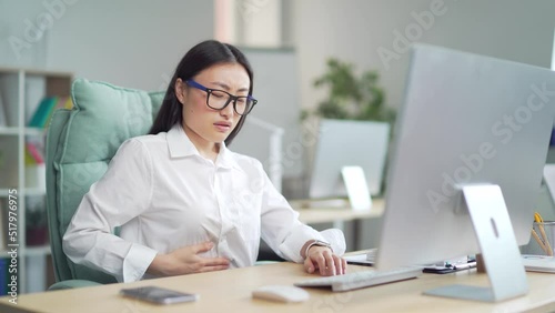 Young Asian woman worker, employee entrepreneur with stomach pain, poisoning, Premenstrual syndrome, heaviness in abdominal Suffering sitting at workplace at work in office at computer desk. Indoor