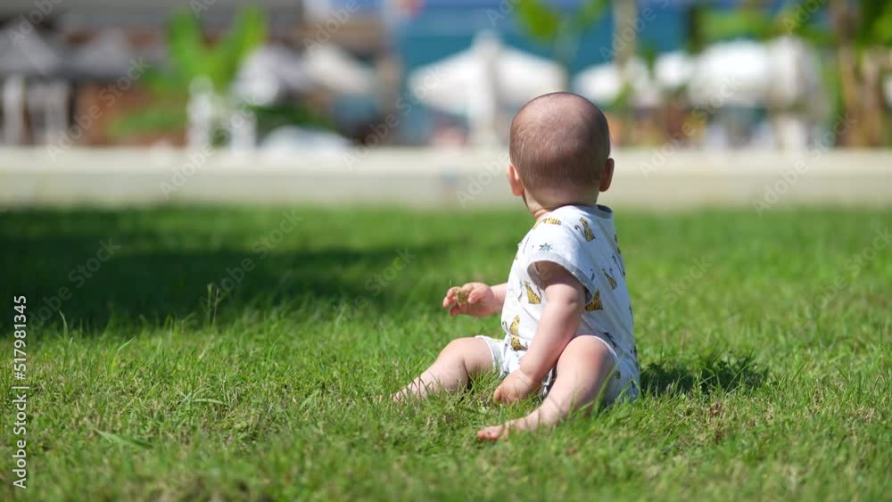 Cute baby boy sitting on the green grass and crawling summer day