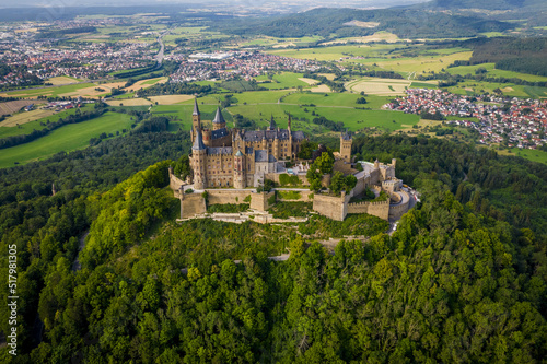 Drone shot of Hohenzollern Castle on forested mountain top in the Swabian Alps in summer. Scenic aerial view of old German Burg. Famous fairytale Gothic landmark in Stuttgart vicinity © Defree