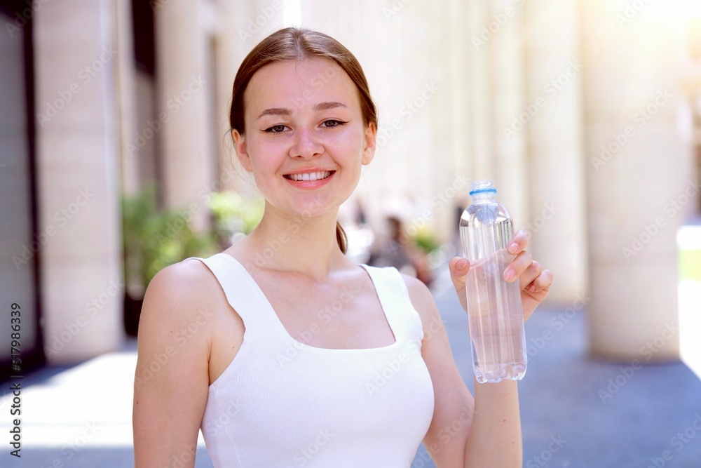 Portrait of beautiful teenager pretty girl, young happy thirsty woman is drinking pure fresh water from bottle at warm sunny summer day outdoors smiling looking at camera Portrait of beautiful teenager pretty girl, young happy thirsty woman is drinking pure fresh water from bottle at warm sunny summer day outdoors smiling looking at camera