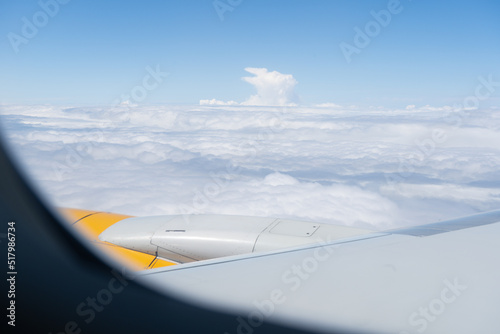 Blue sky and white clouds from plane window during the flight. Yellow aircraft wing and turbine
