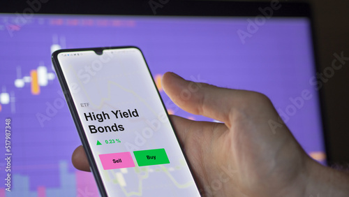 An investor's analizing the high yield bonds etf fund on a screen. A phone shows the prices of High Yield Bonds