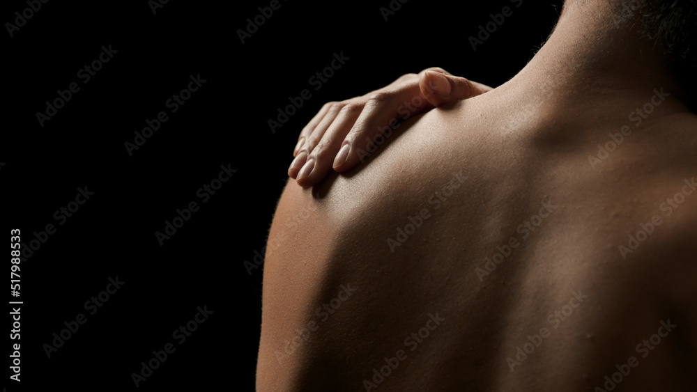 Fototapeta premium Horizontal close-up shot of young good-looking slim African American woman touches her bare shoulder on black background | Body care concept