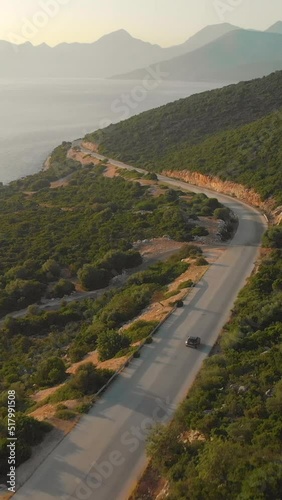 AERIAL: Beautiful shot of the stunning Mediterranean nature and the tranquil sea surrounding the car cruising around Lefkas on a sunny summer morning. Idyllic shot of car on road trip across Lefkada.