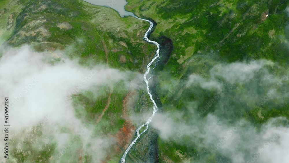 Aerial top view of nordic landscape, flyover green valley beautiful formations, flight through rainy clouds. Cinematic drone shot of amazing north fjord small lake and winding river in Iceland