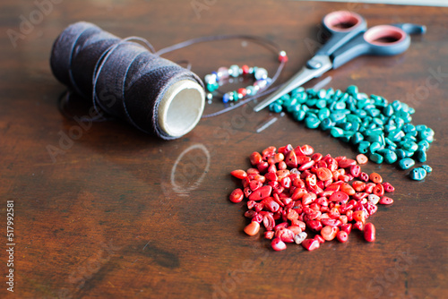 red and turquoise semiprecious stones on wooden table with waxed thread and scissors photo