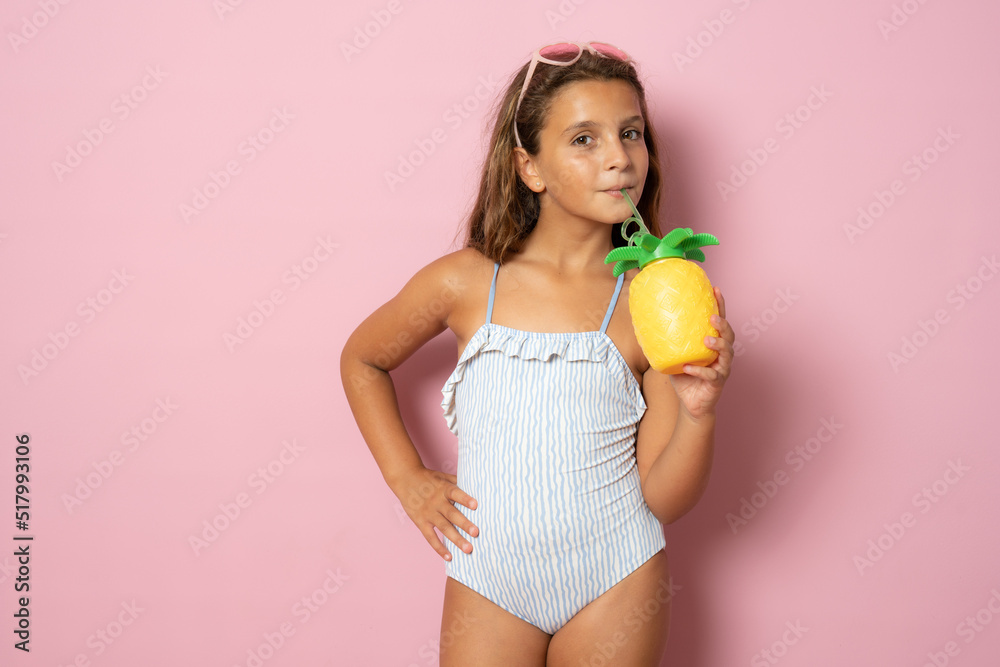 Cute child girl wearing swimsuit in summer holidays over pink background holding a pineapple with sunglasses Cute child girl wearing swimsuit in summer holidays over pink background holding a pineapple with sunglasses