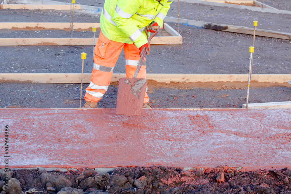 Builder spreading poured concrete with a shovel. A construction worker is placing tinted concrete into formwork Builder spreading poured concrete with a shovel. A construction worker is placing tinted concrete into formwork