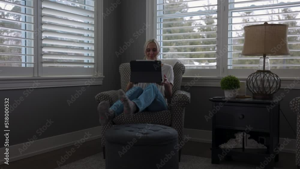 Woman walking to a chair in a corner nook to scroll through her tablet and drink coffee in nice clothes with warm weather feels with a lower angle. Woman walking to a chair in a corner nook to scroll through her tablet and drink coffee in nice clothes with warm weather feels with a lower angle.
