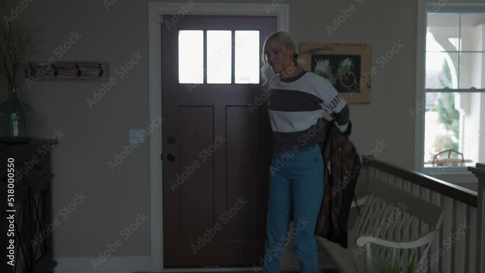 woman coming in from outside through the front door with a coat on due to the cold weather. Taking off her jacket then shoes. woman coming in from outside through the front door with a coat on due to the cold weather. Taking off her jacket then shoes.