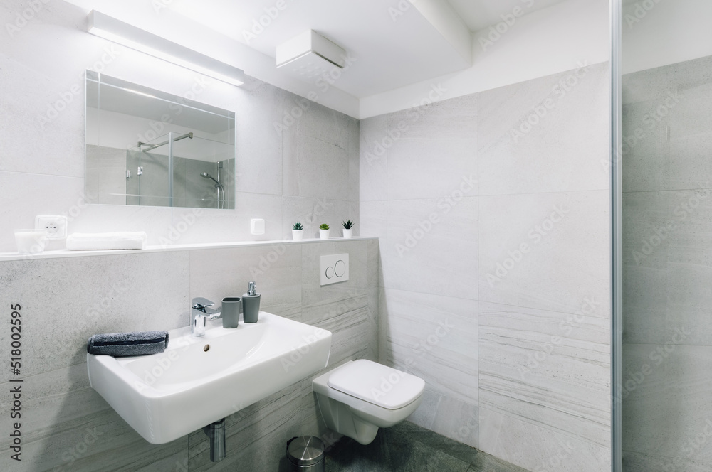 Small simple bathroom with mirror. Bathroom has square sink and shower with glass door and toilet with seat closed. There are also some additional items as bin, dispenser, towel, etc. Small simple bathroom with mirror. Bathroom has square sink and shower with glass door and toilet with seat closed. There are also some additional items as bin, dispenser, towel, etc.