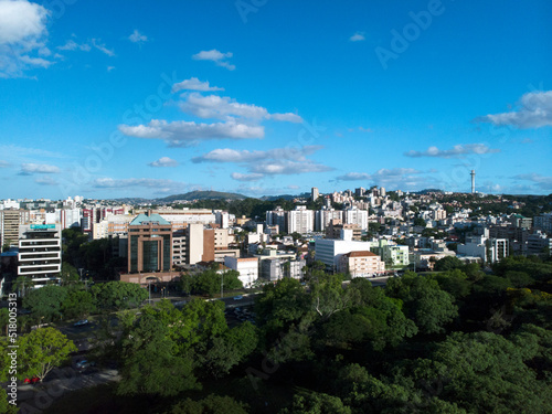 Aerial view of residential buildings next to a park, with many trees, in the background a hill with antennas.