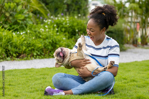 Foto African American woman is playing with her french bulldog puppy while walking in