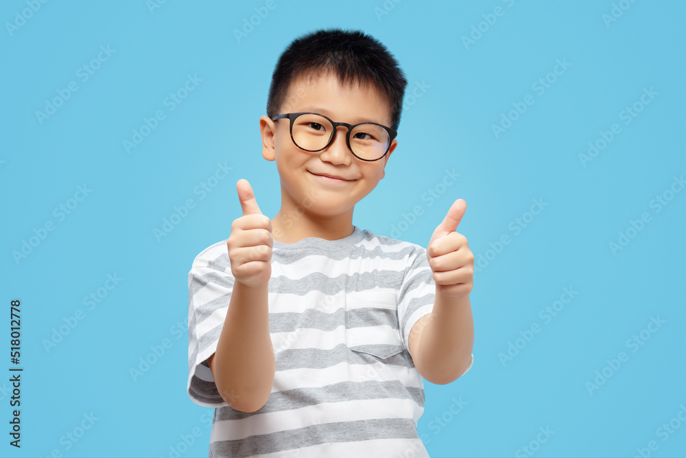 Happy kid showing thumbs up, wearing eyeglasses on blue background Happy kid showing thumbs up, wearing eyeglasses on blue background