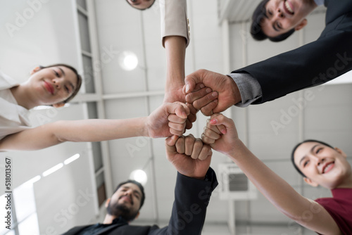 Team building concept. Coworkers standing in circle bumping fist together, celebrating business success in modern office with high ceiling. Bottom View