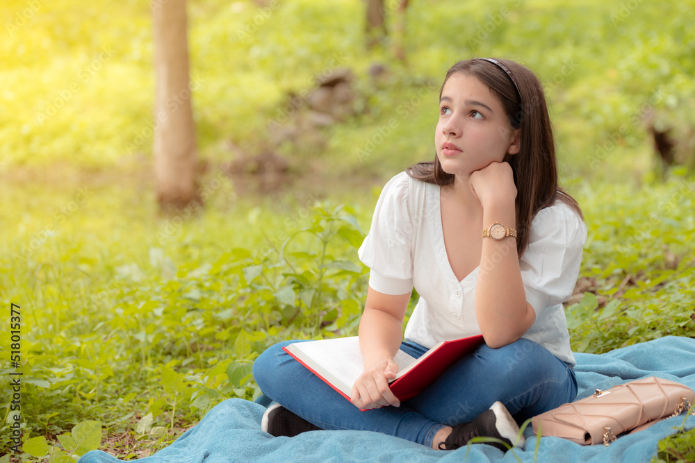 young girl with high hopes sitting in the forest reading a book on a blue blanket young girl with high hopes sitting in the forest reading a book on a blue blanket