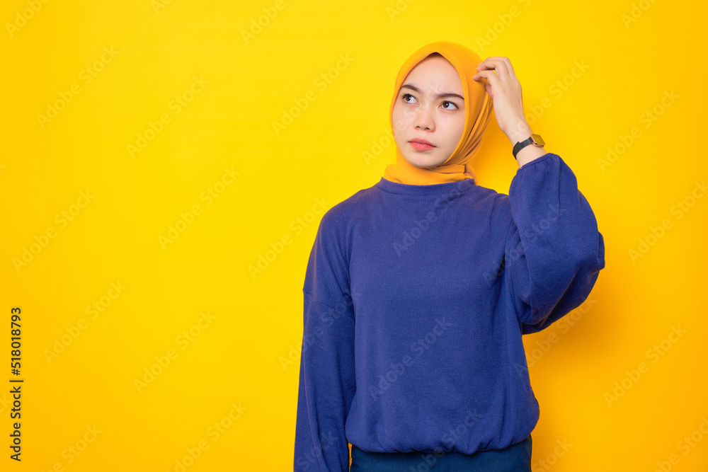 Pensive young Asian Muslim woman dressed in casual sweater looking up at copy space and touching chin, thinking about interesting offer isolated over yellow background Pensive young Asian Muslim woman dressed in casual sweater looking up at copy space and touching chin, thinking about interesting offer isolated over yellow background