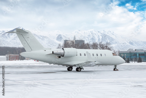 White luxury executive airplane on the winter airport apron on the background of high scenic mountains