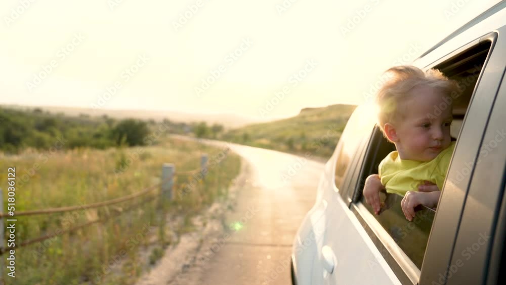 Teen boy looking out the car window and waving his hand. Family travel by car. Hand to wind of freedom. Cheerful boy smiles. Happy family concept. Boy in the car window. The wind of freedom at sunset Teen boy looking out the car window and waving his hand. Family travel by car. Hand to wind of freedom. Cheerful boy smiles. Happy family concept. Boy in the car window. The wind of freedom at sunset