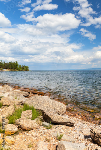 Summer landscape of Lake Baikal on a sunny day. In the distance near the forest is a tent camp for autotourists. Natural background. Summer outdoor recreation and fishing photo