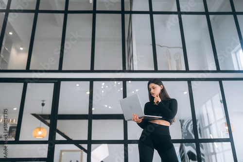 Young woman in a sports suit standing holding a laptop in her hands