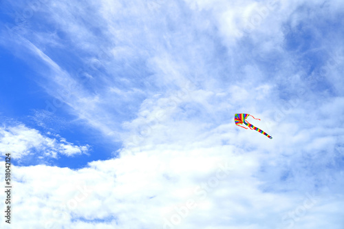 Rainbow kite flying in blue sky with clouds