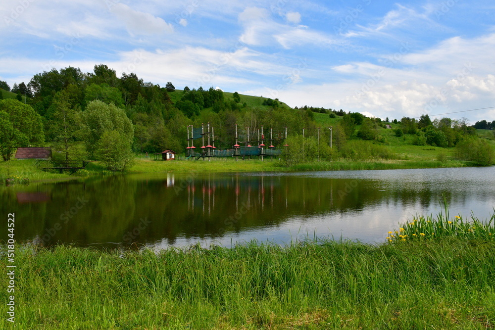 A view from the top of a tall hill or mountain with vast fields, meadows, forests, moors, and other types of flora visible, with a lake, some urban settlements, and other buildings in the distance A view from the top of a tall hill or mountain with vast fields, meadows, forests, moors, and other types of flora visible, with a lake, some urban settlements, and other buildings in the distance