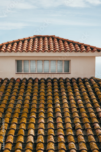 Roof of a house with small window and terracotta tiles.