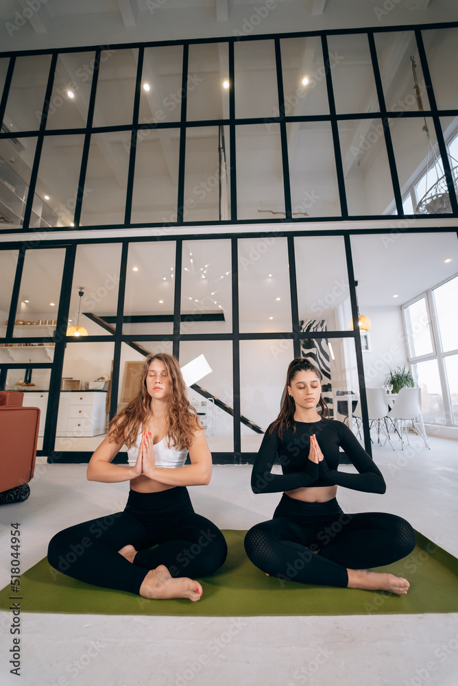 Two young women meditating in lotus pose with hands in namaste.