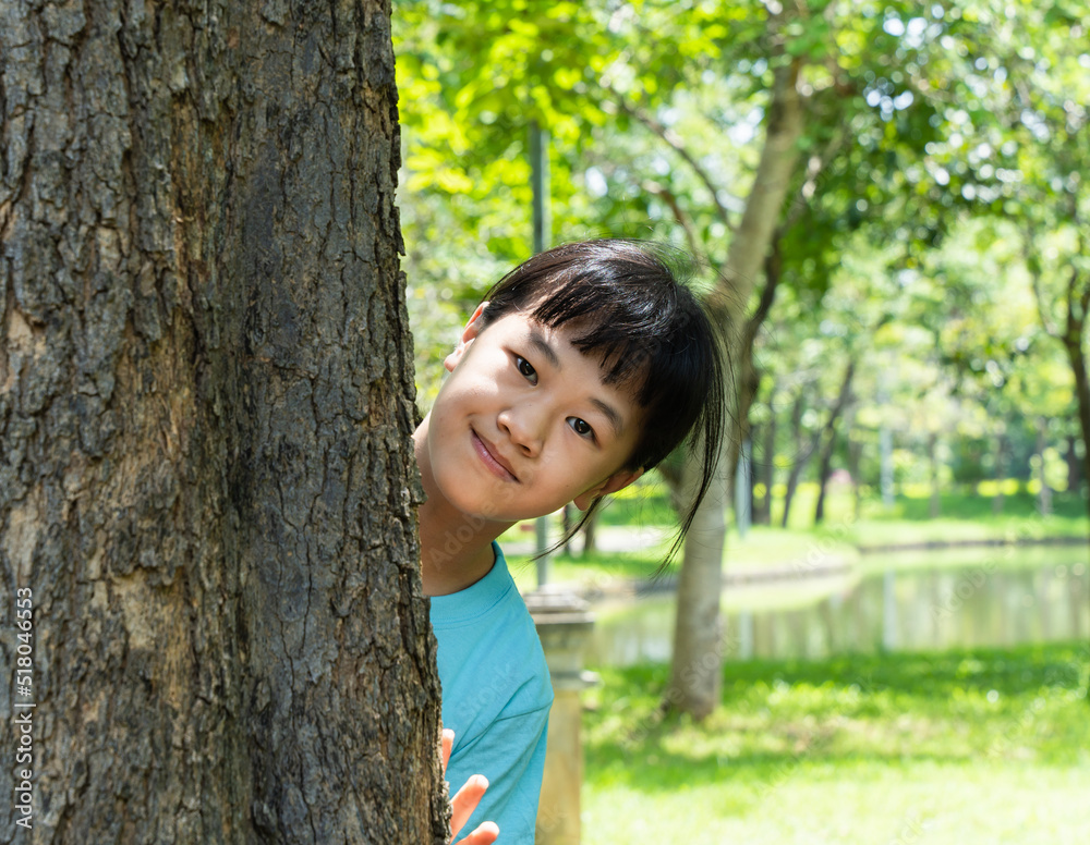 Pretty little girl peeking out from behind a tree. Portrait of child girl enjoying summer day in the green park. Pretty little girl peeking out from behind a tree. Portrait of child girl enjoying summer day in the green park.