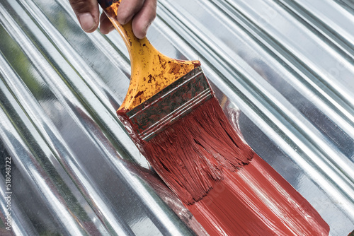 Painting the surface of a sheet of Galvanized Iron or GI corrugated metal with rust inhibiting red oxide primer. photo