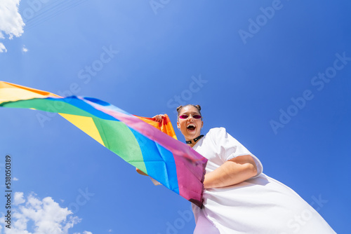 A young woman develops a rainbow flag against the sky © teksomolika