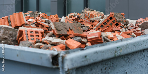 Red bricks debris in construction metal waste container close up. Building demolition and remove. photo