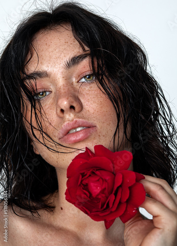 beauty young woman face with a lot of freckles and natural lips, red rose near face, close up