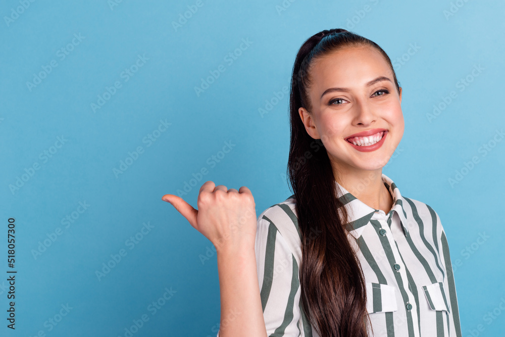 Smiling business woman pointing finger at copy space wear fashion shirt isolated over blue wall background Smiling business woman pointing finger at copy space wear fashion shirt isolated over blue wall background