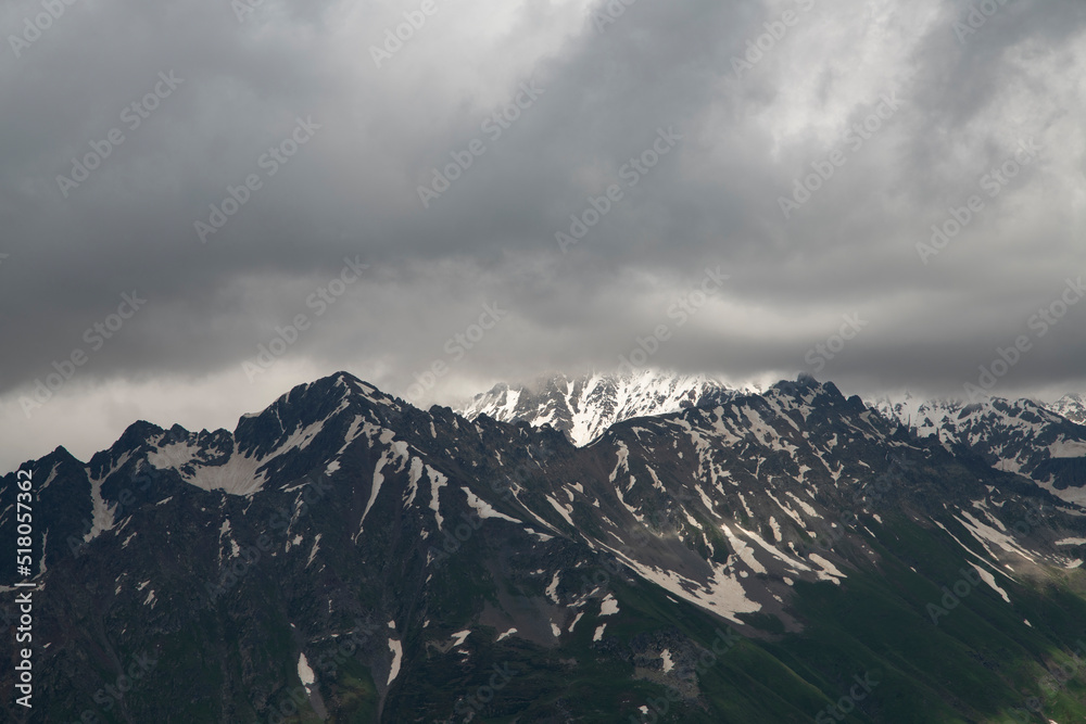 Mountains landscape. High snow covered mountains in the fog and clouds, dramatic sky. 