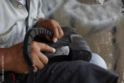 Cut the edges of the treads that have been replaced by rubber treads using a cutter. Isolated on a shoe repairman manually. Isolated on Repairing broken shoes by a shoe repairman.
