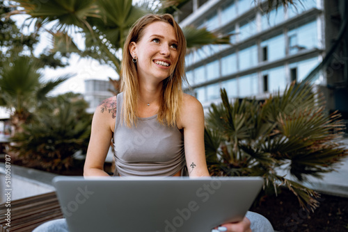 Young beautiful casual woman working on a laptop sitting on the bench in the street