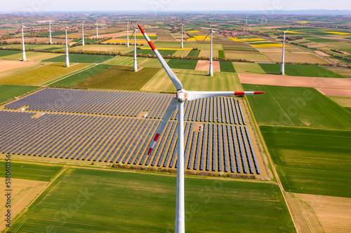 Generation of green energy in Germany by solar panels of a solar park and wind turbines up to the horizon as an aerial view