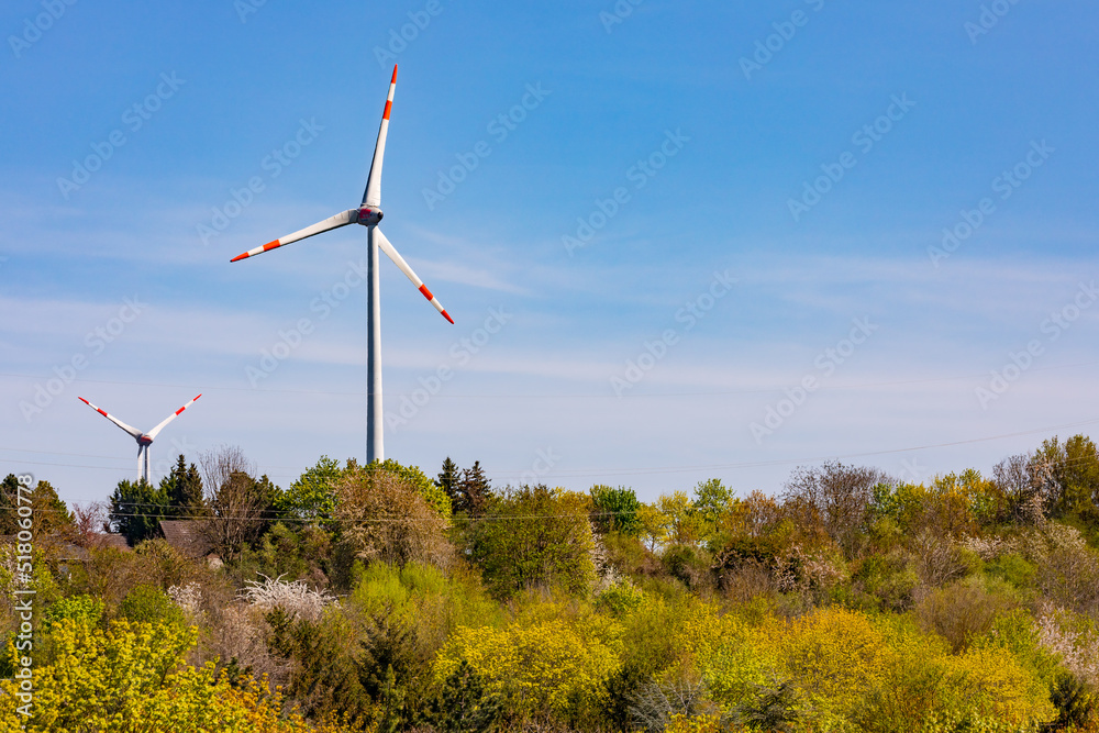 Windräder und Sträucher am Rand einer Siedlung vor blauem Himmel Windräder und Sträucher am Rand einer Siedlung vor blauem Himmel