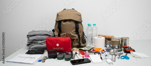 Emergency backpack equipment organized on the table. Documents, water,food, first aid kit and another items needed to survive.